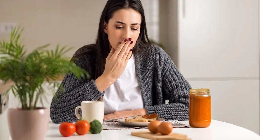 Pregnant woman looking disgusted at a plate of food